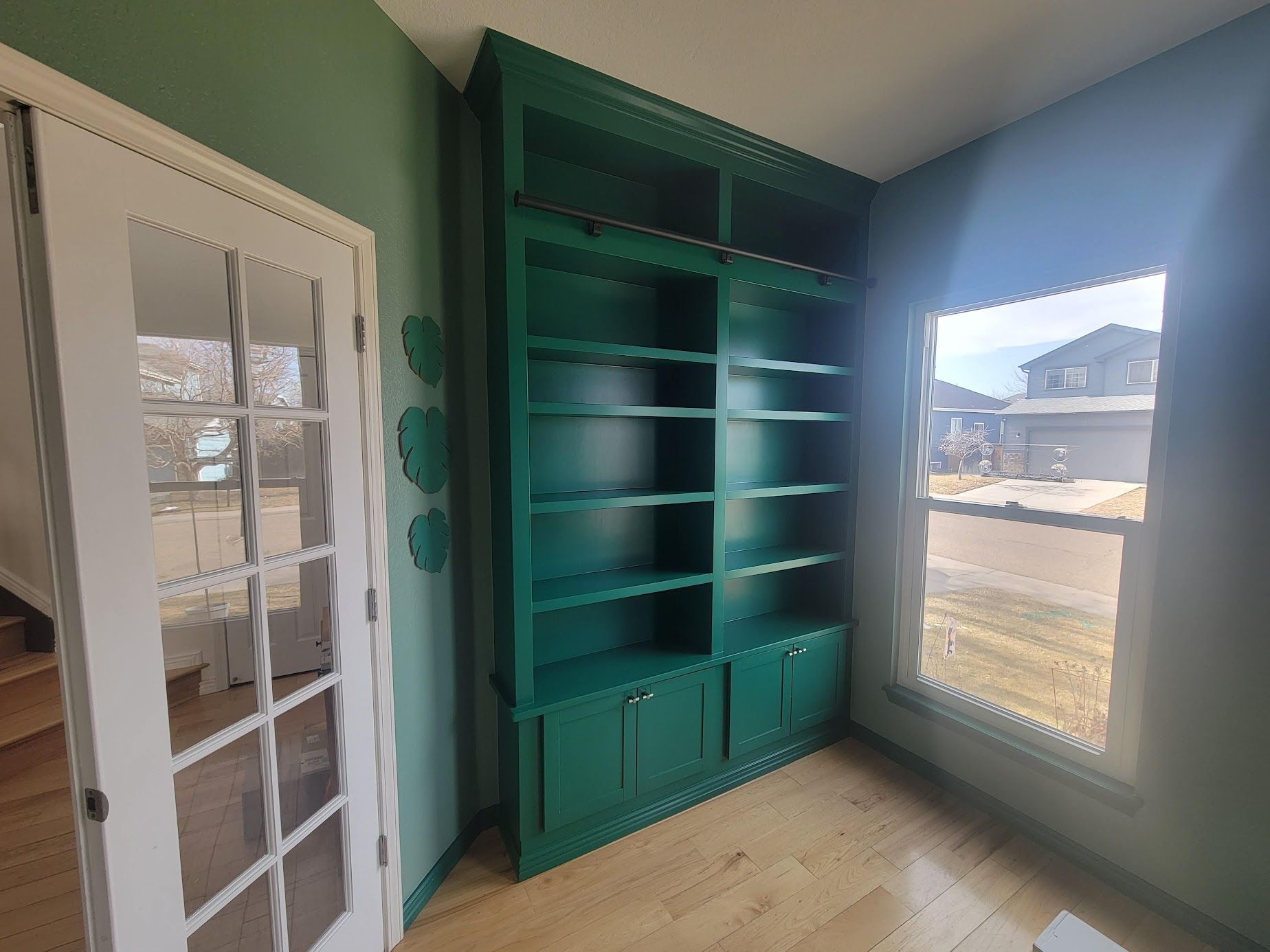 Teal built-in shelves and cabinet in a bright room beside a white French door and window.