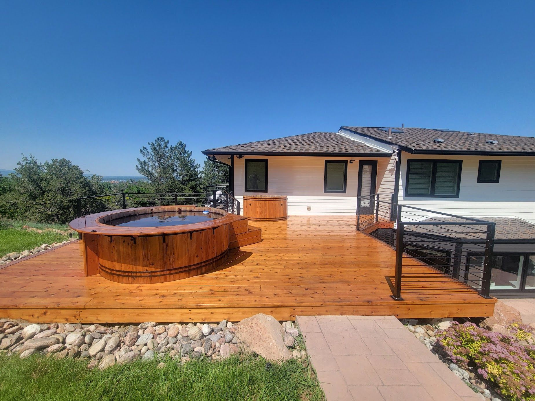 Wooden deck with a round hot tub beside a house under a clear blue sky