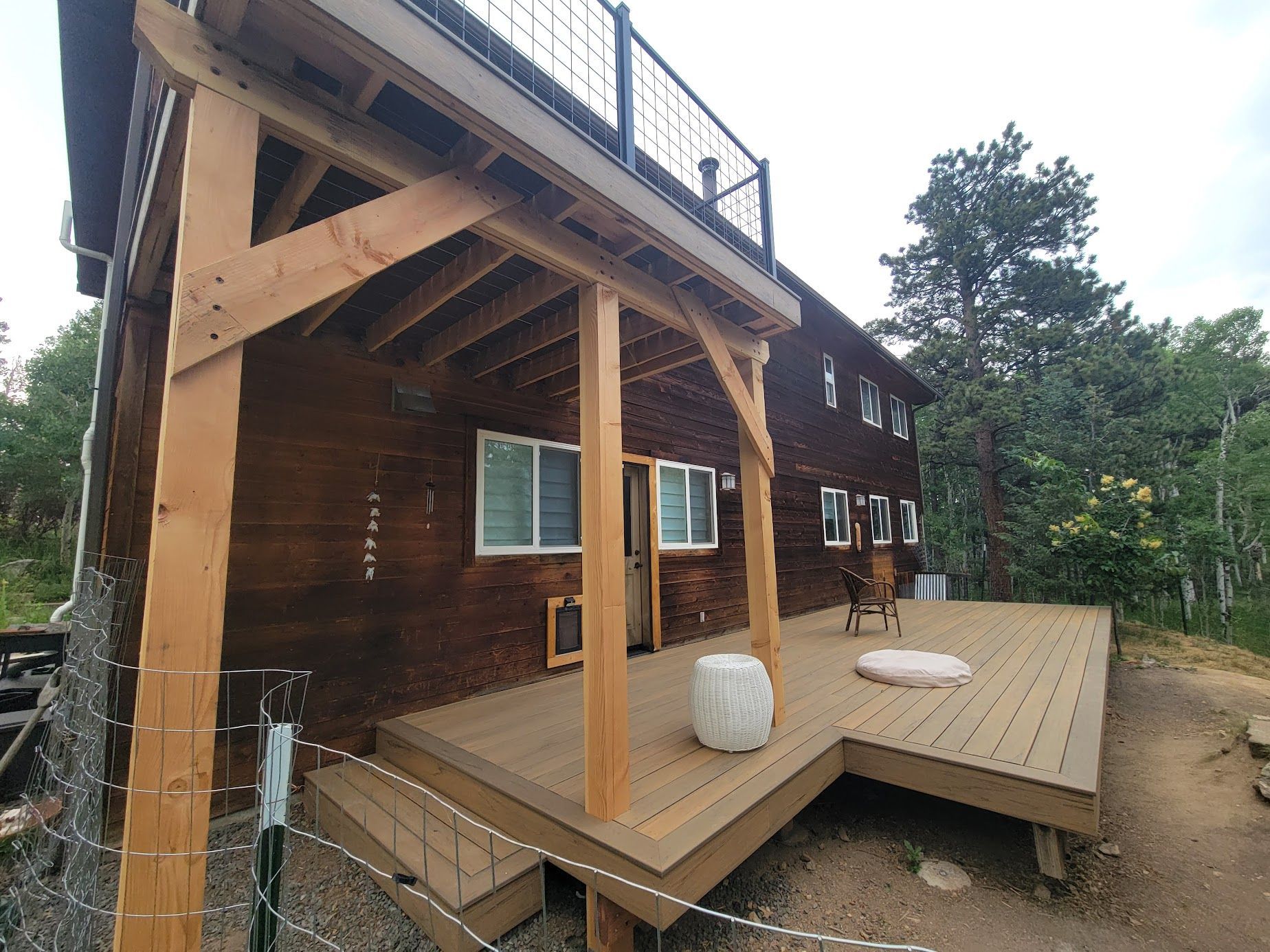 Wooden cabin deck with stairs, railing posts, and forest view under cloudy sky