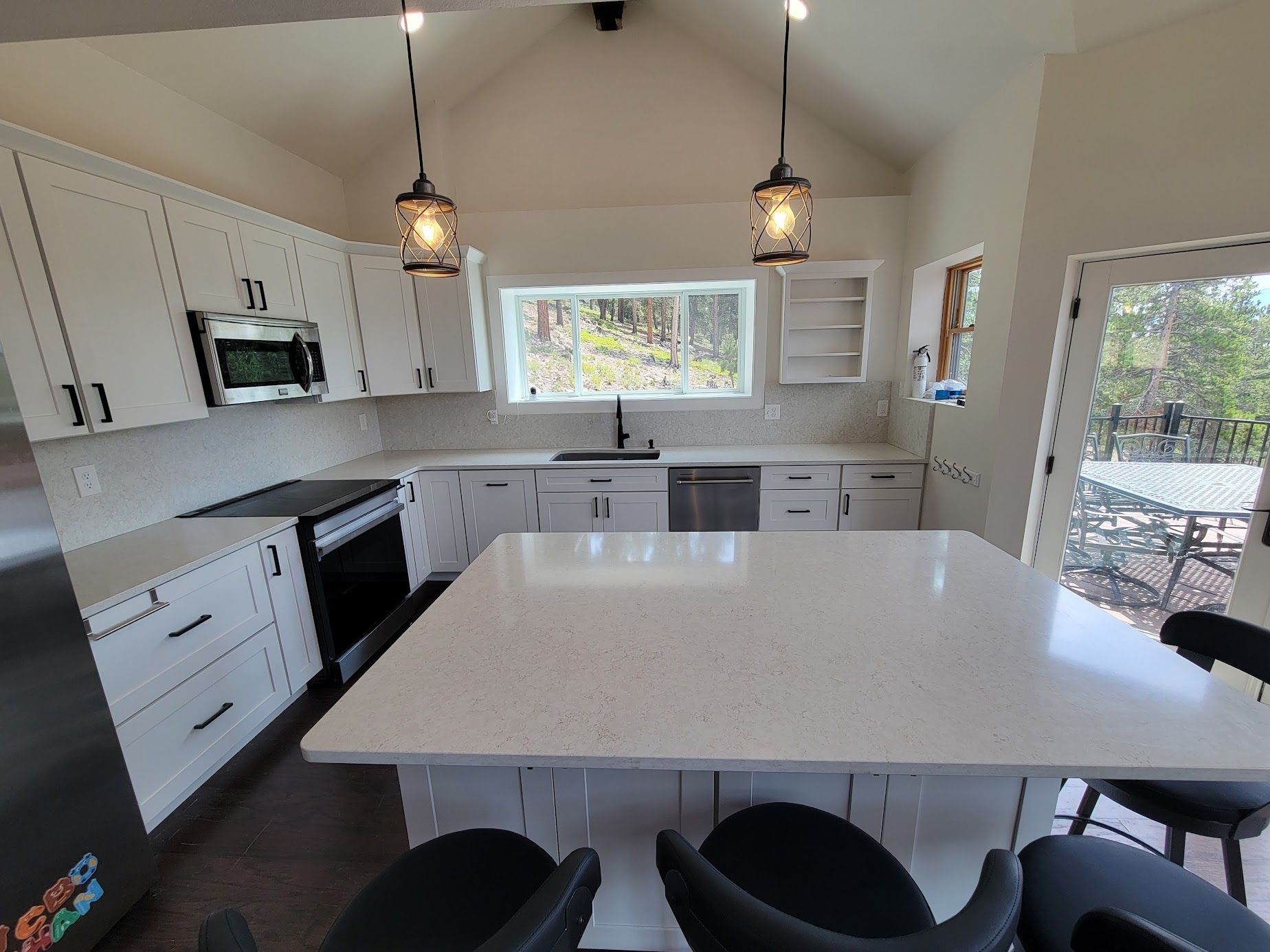 Bright modern kitchen with white cabinets, black island stools, and pendant lights under a large window