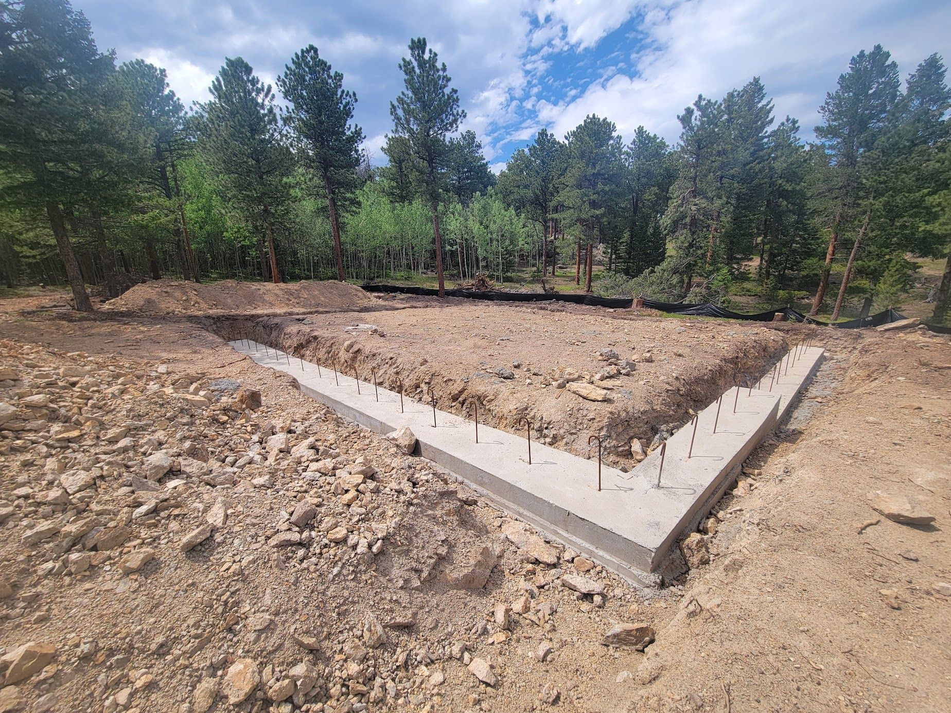 Concrete foundation slab in a dirt clearing with trees and blue sky in the background