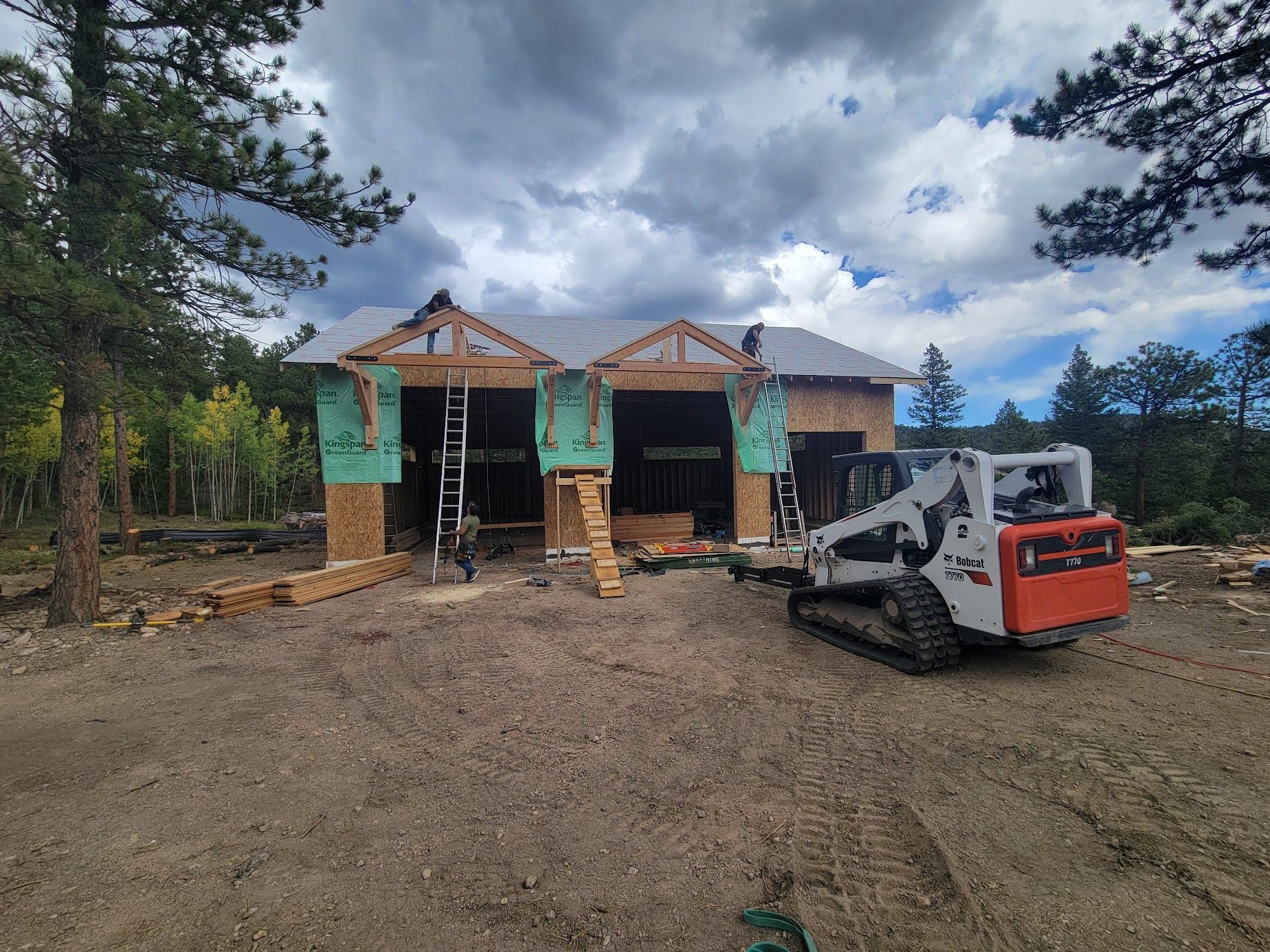 Construction site with a wooden house frame and a compact loader on a dirt lot under cloudy skies