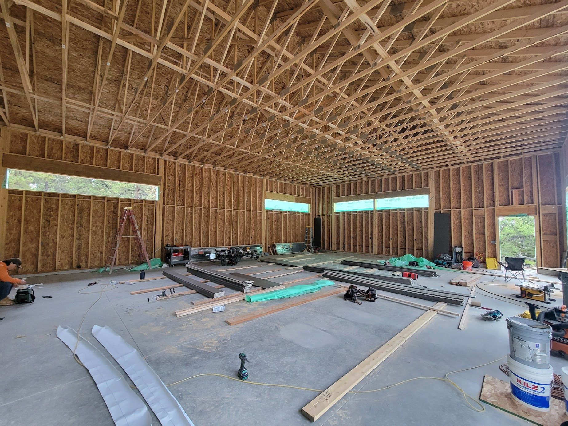 Unfinished wooden building interior with exposed framing, scattered tools, and construction materials on the floor
