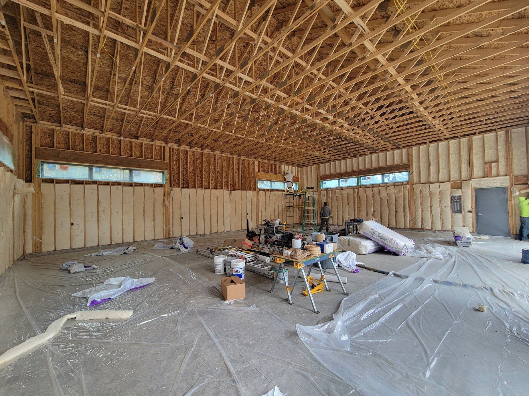 Unfinished wood-framed interior with exposed trusses, insulation, tools, and construction materials on the floor