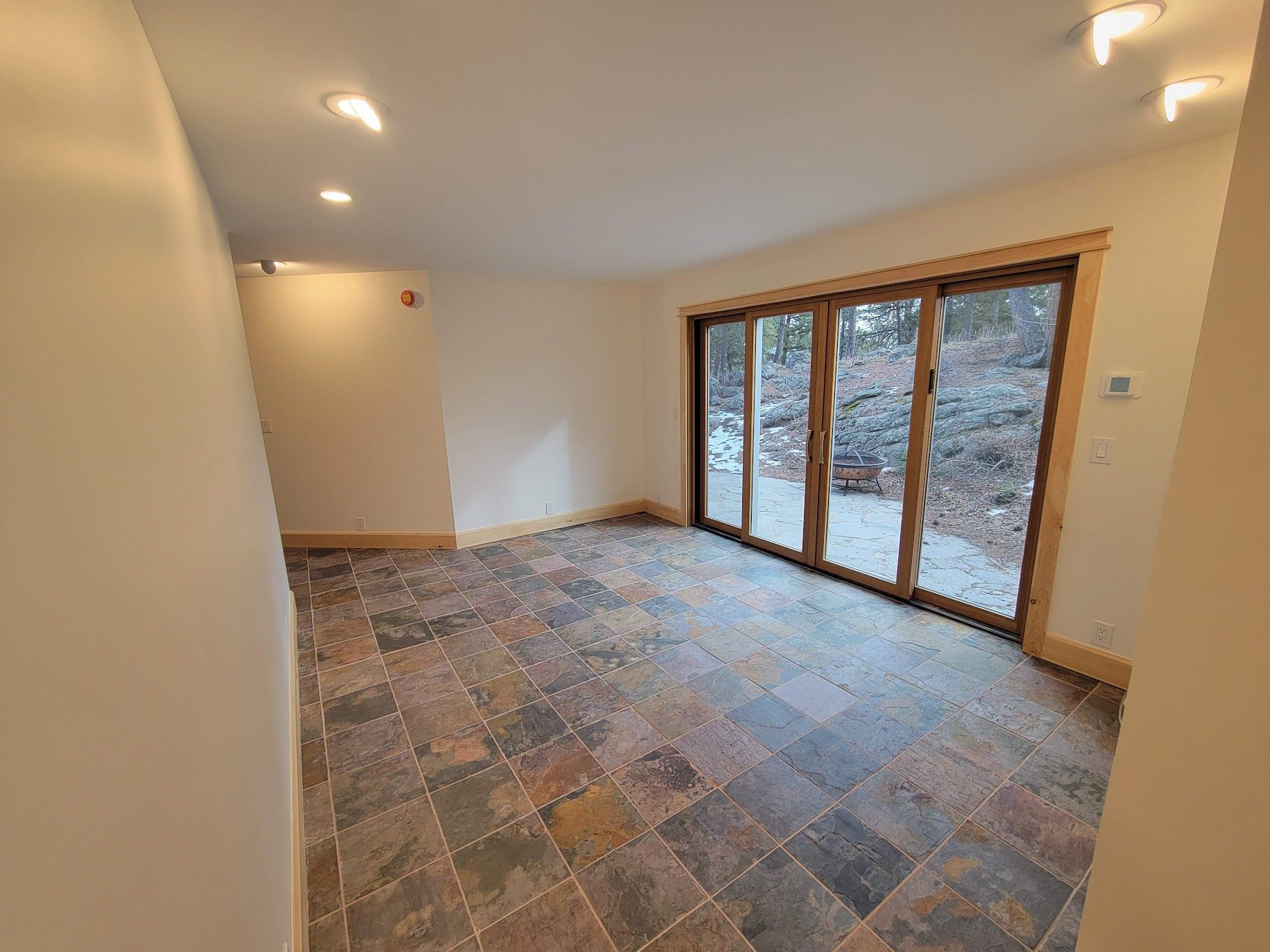 Empty modern room with stone tile floor, recessed lights, and large glass doors overlooking trees