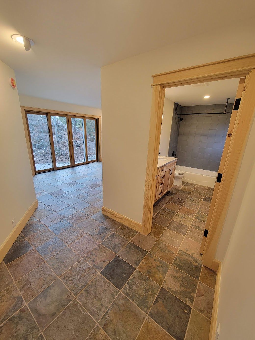 Empty apartment hallway with tiled floor, wood-trimmed doorway, and a bathroom visible to the right.