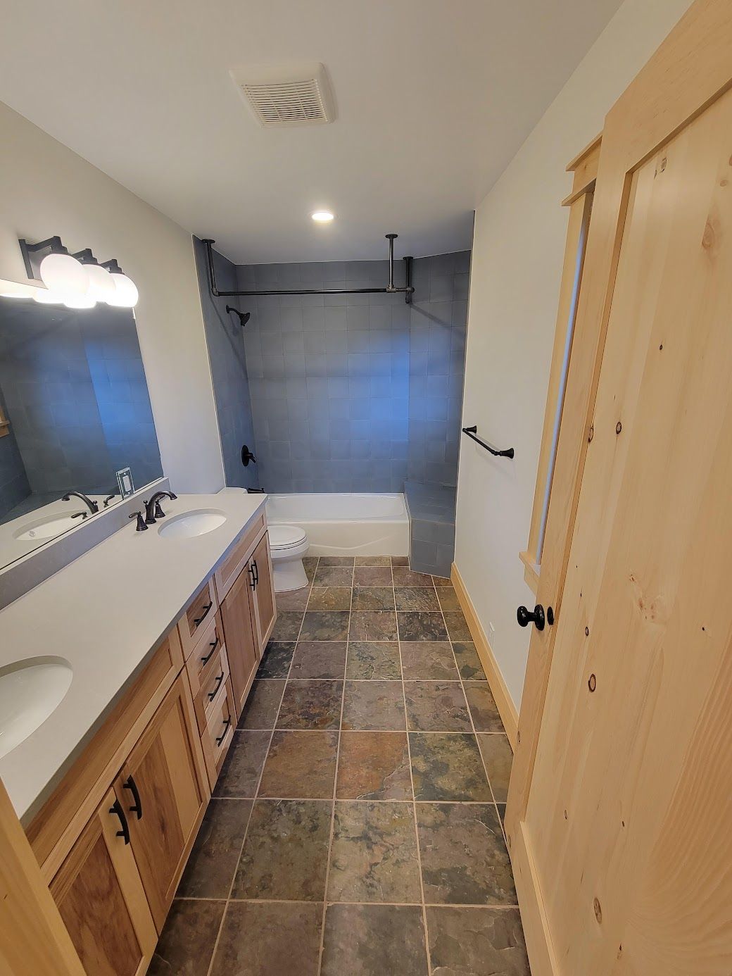 Narrow bathroom with tiled floor, vanity sink, mirror, and bathtub with gray shower curtain.