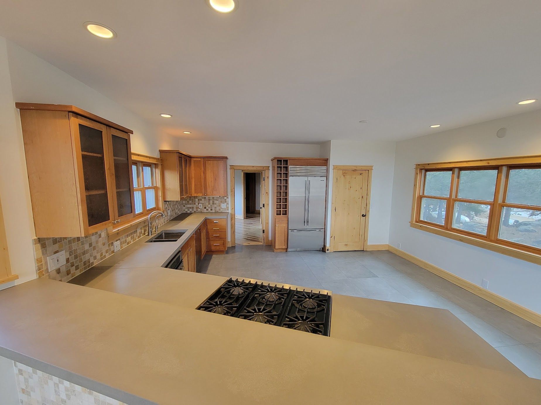 Spacious modern kitchen with wood cabinets, island, and large windows overlooking snow outside