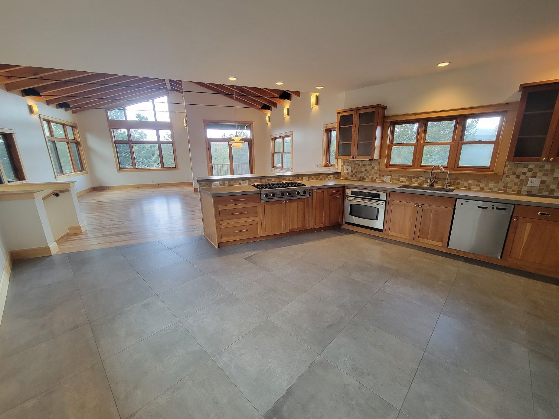 Open kitchen with wood cabinets, island, large windows, and tiled floor.