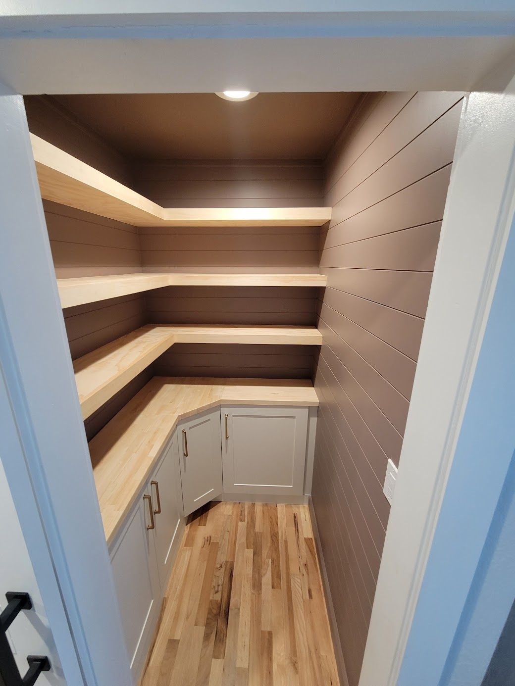 Small walk-in closet with wooden shelves, cabinet doors, and a wood floor.