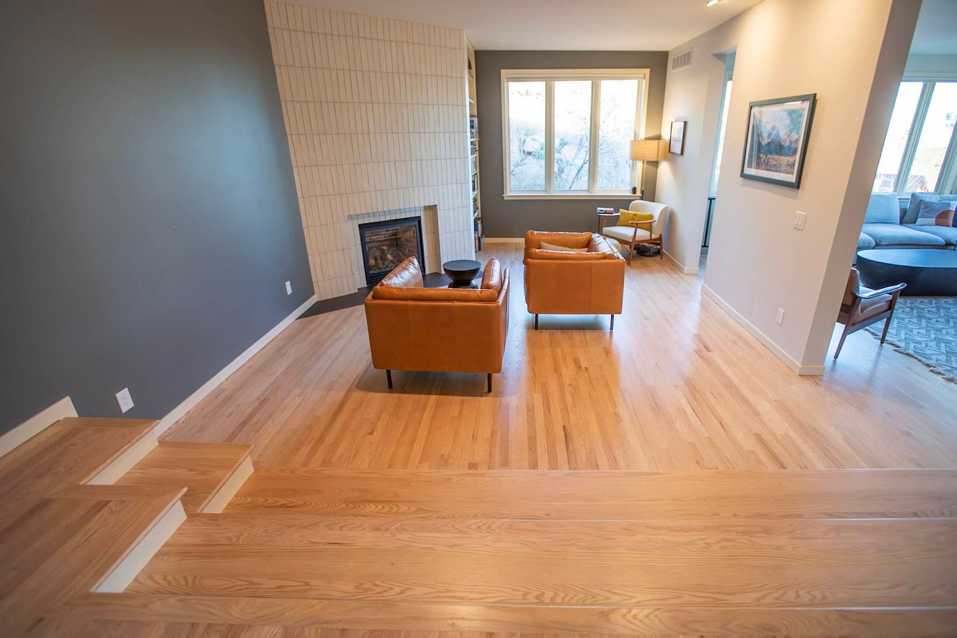 Modern living room with hardwood floors, fireplace, orange chairs, and large windows