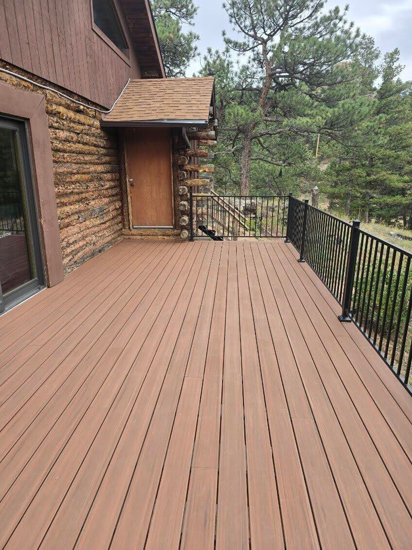 Wooden deck beside a log house, with a railing and forest view