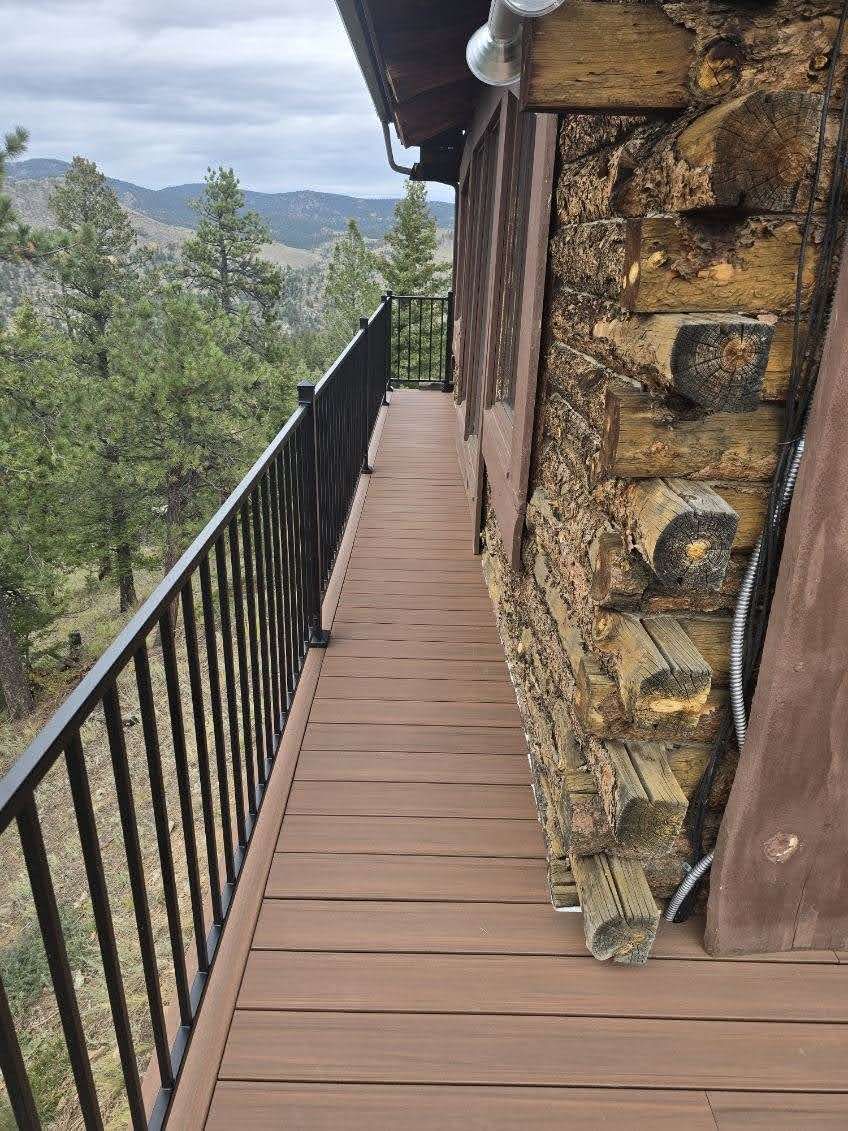 Narrow wooden balcony beside a stone wall, overlooking a forested mountain view.