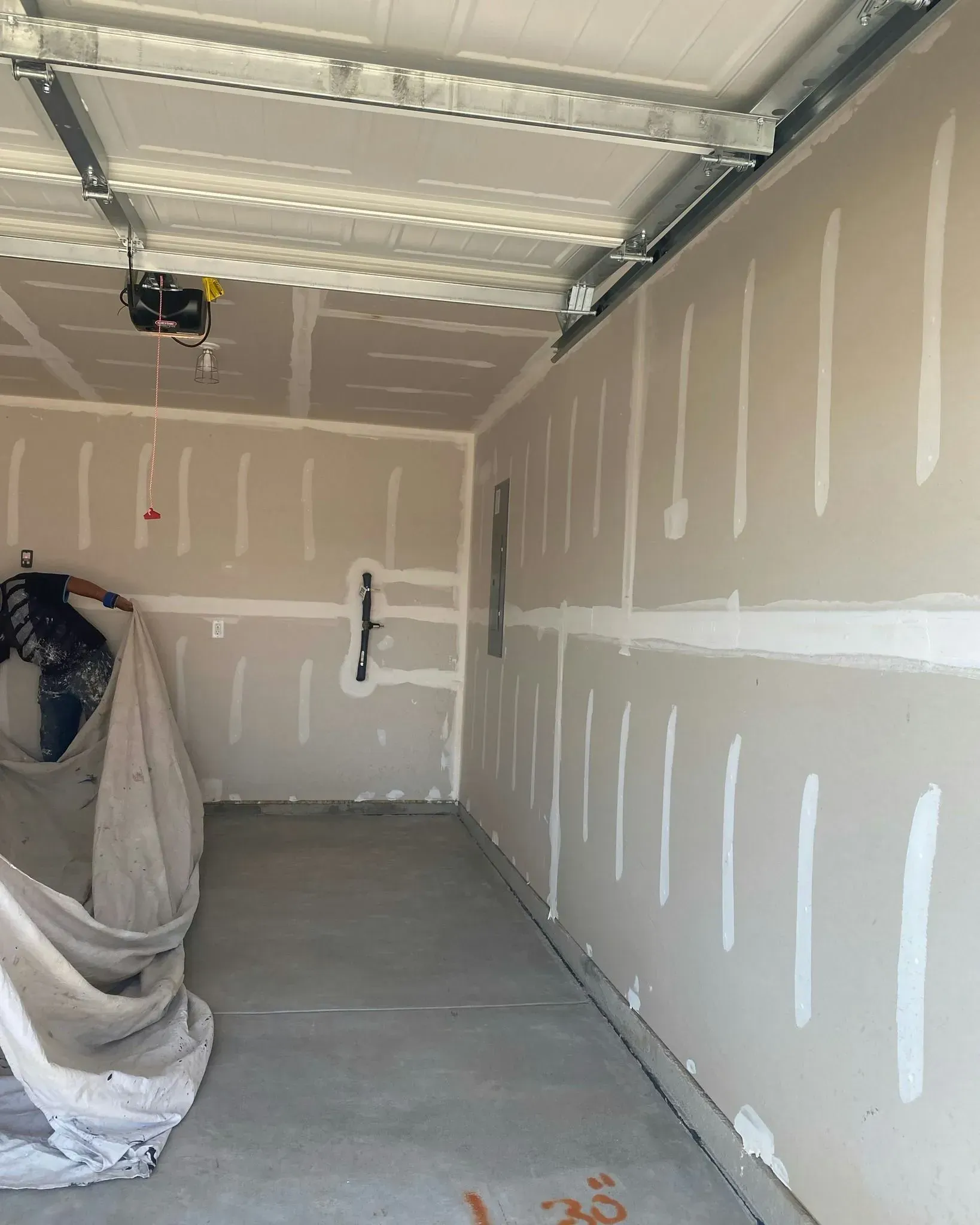 Empty unfinished garage interior with drywall seams, concrete floor, and a partially covered item on the left