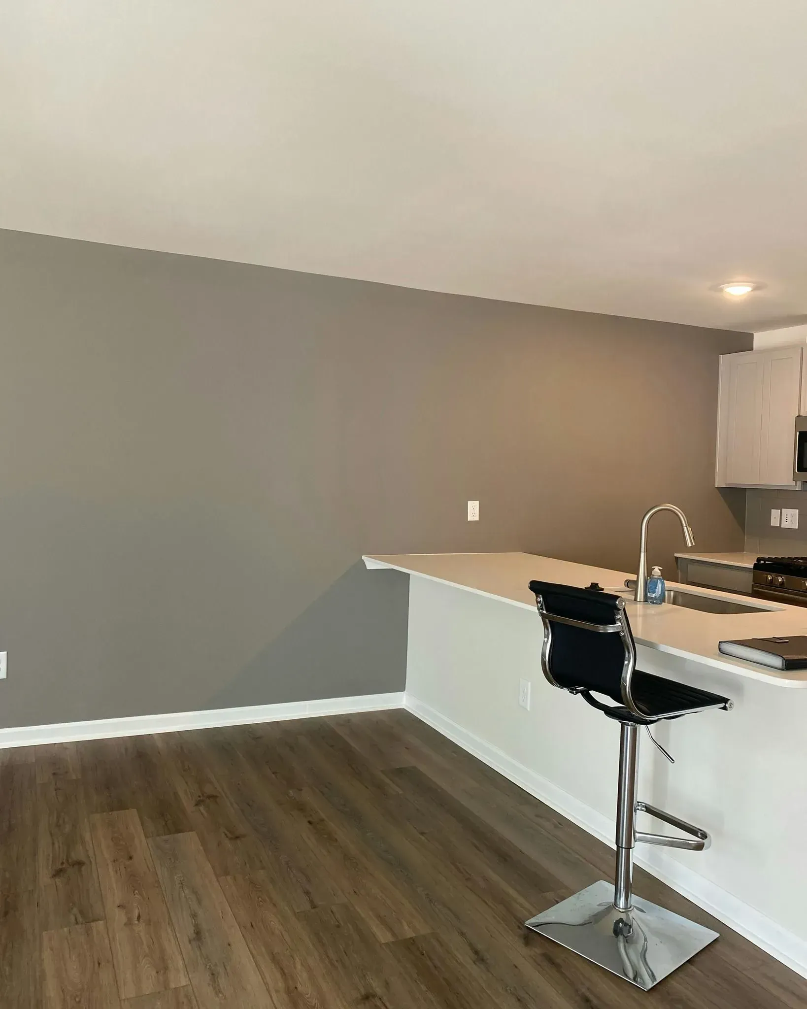 Empty modern kitchen with gray wall, wood floor, white cabinets, and a breakfast bar with a stool