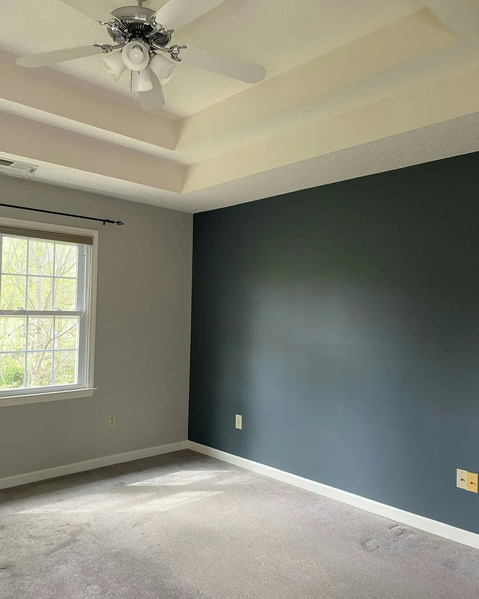 Empty bedroom with light gray walls, dark accent wall, window, carpet, and ceiling fan.