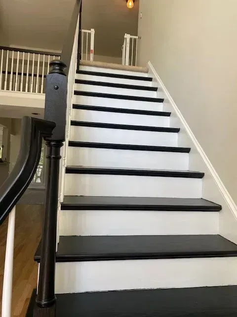 White staircase with black treads and a dark handrail in a home interior.