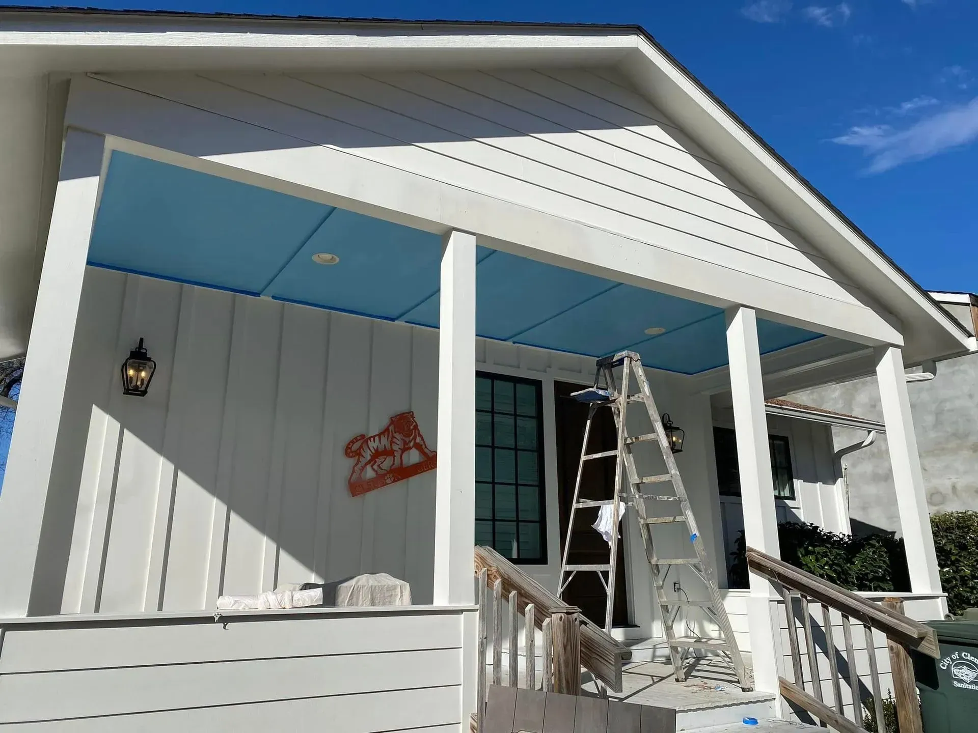 Front porch with white siding, blue ceiling, a ladder, and a red sign on the wall