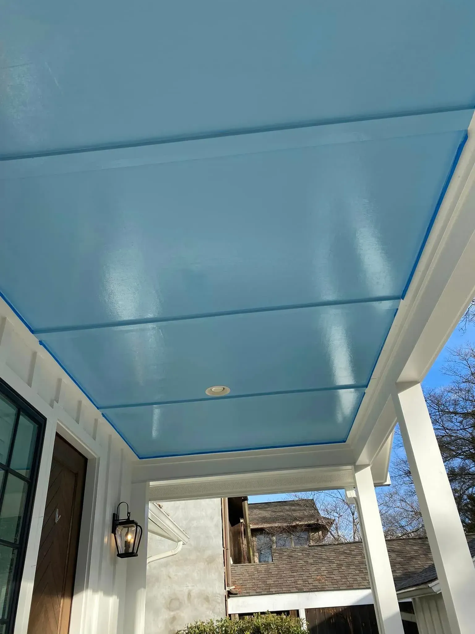 Blue porch ceiling with recessed light, viewed from below beside a house exterior and sky.