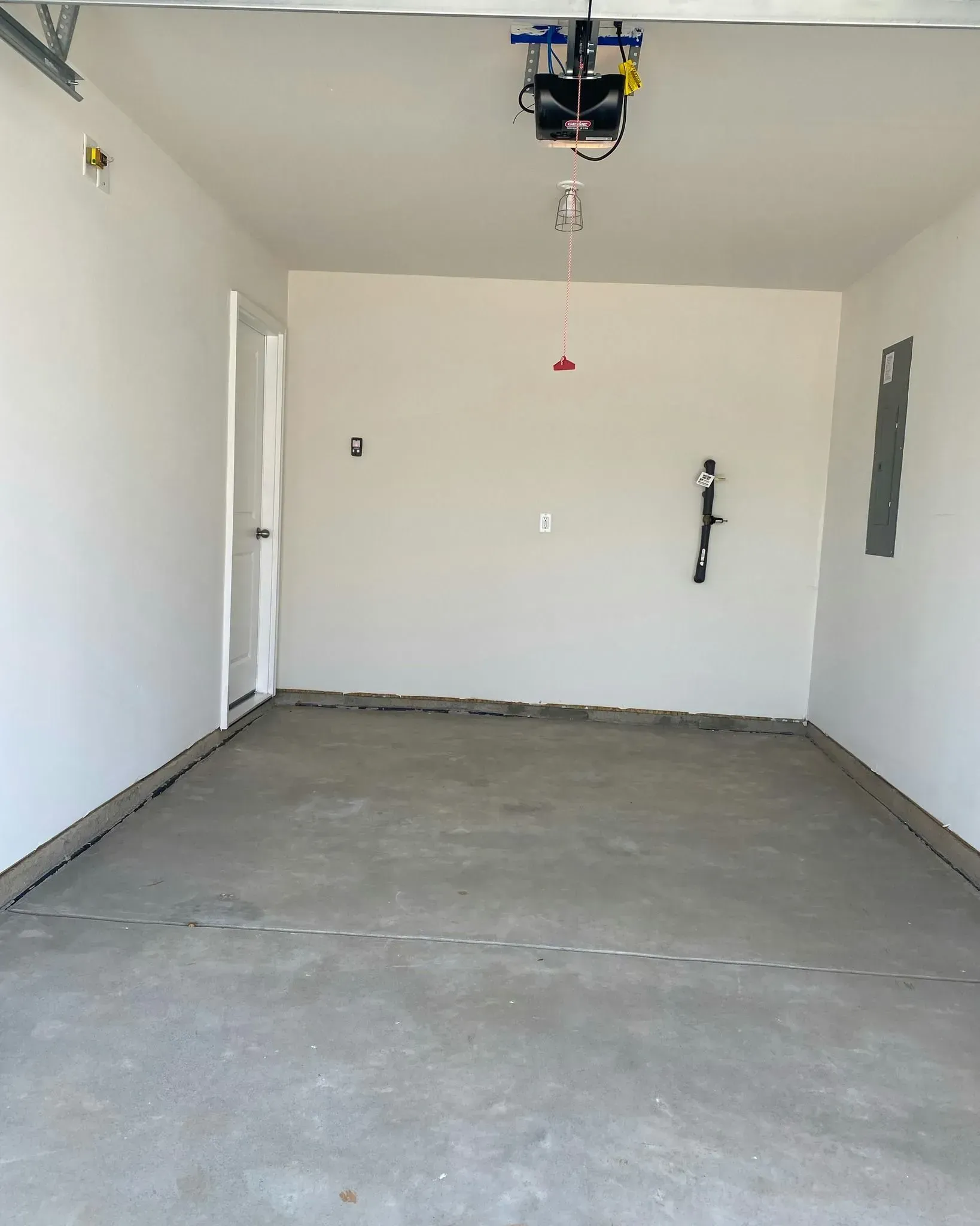 Empty garage with concrete floor, white walls, and an overhead door opener.