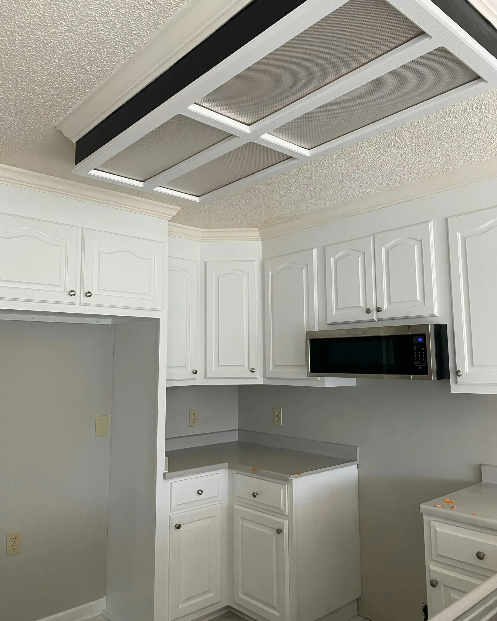 Bright kitchen with white cabinets, gray countertops, and a ceiling light fixture with dark trim.