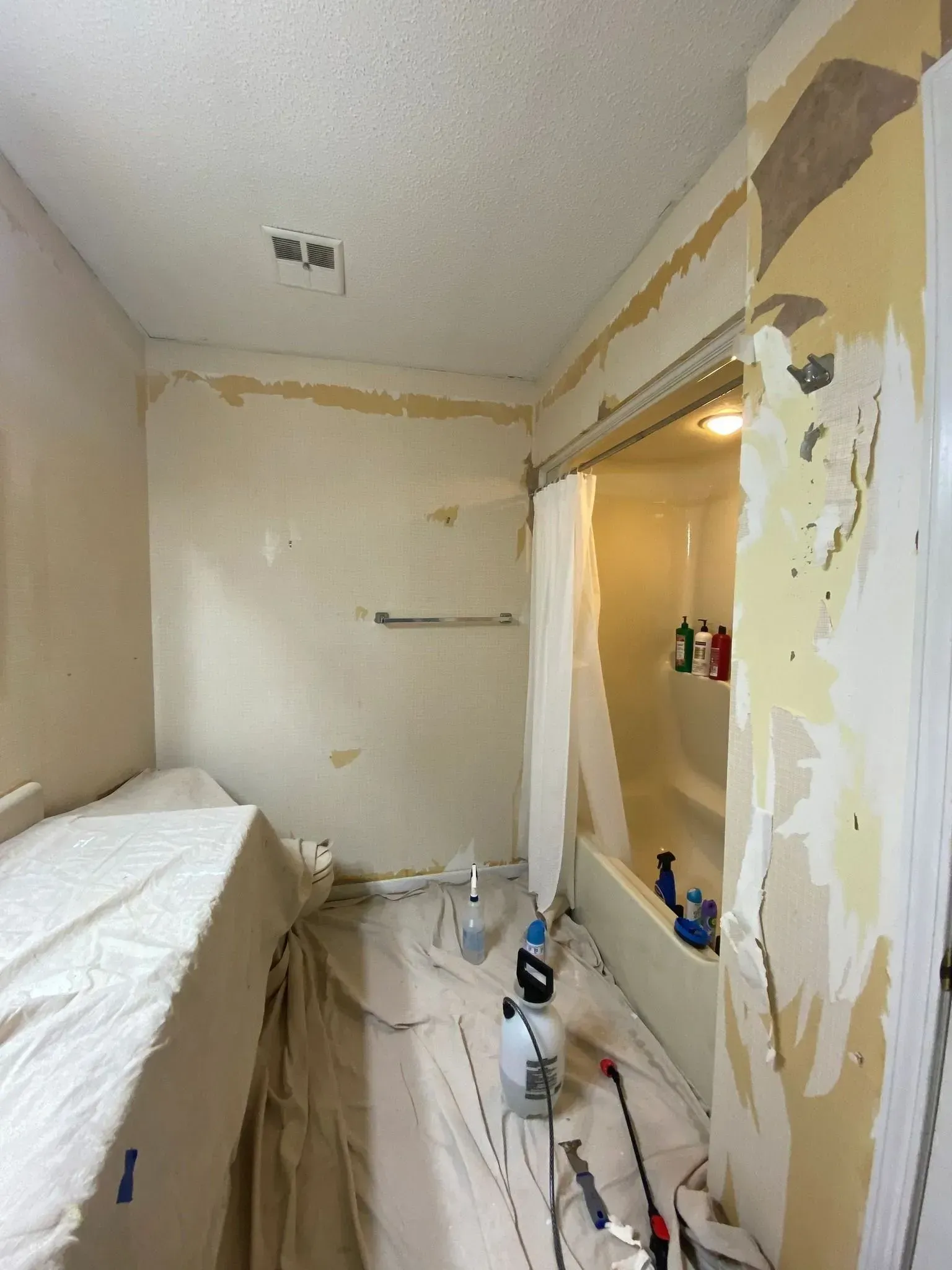 Small room under renovation with peeling paint, exposed patches, and tools on the floor.