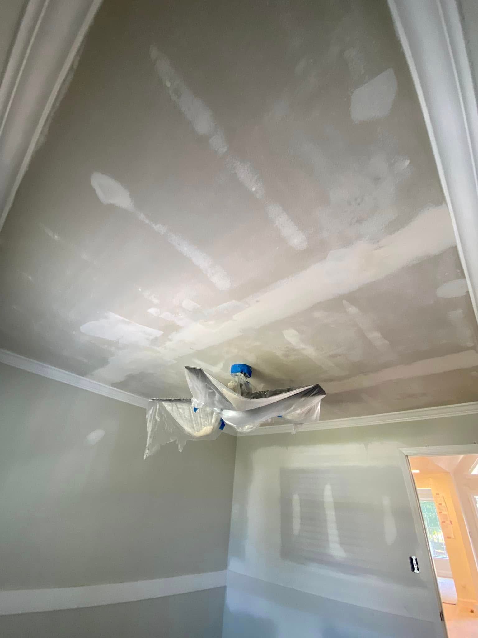 Interior room with drywall ceiling patched and taped, hanging light fixture, and fresh paint lines on the walls