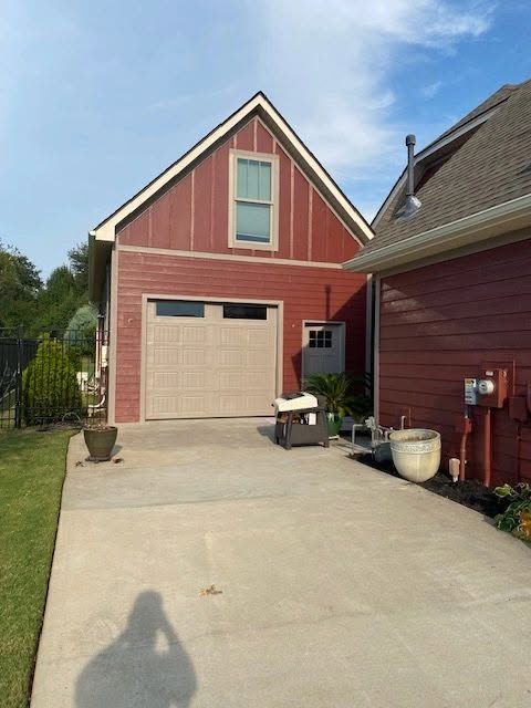 Red house with a beige garage door and driveway, beside a red side wall and potted plants.