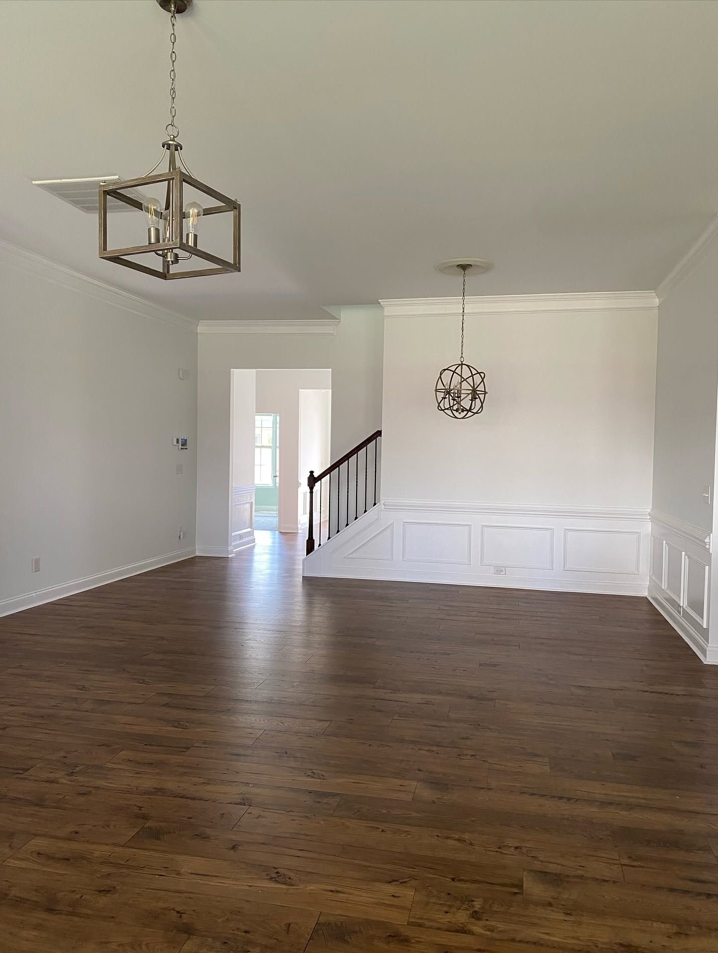 Empty dining room with hardwood floors, white walls, chandelier, and wainscoting leading to a staircase.