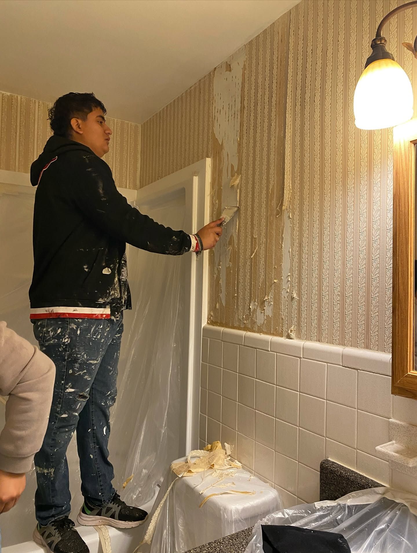 Person painting a striped bathroom wall beside a mirror and sink area