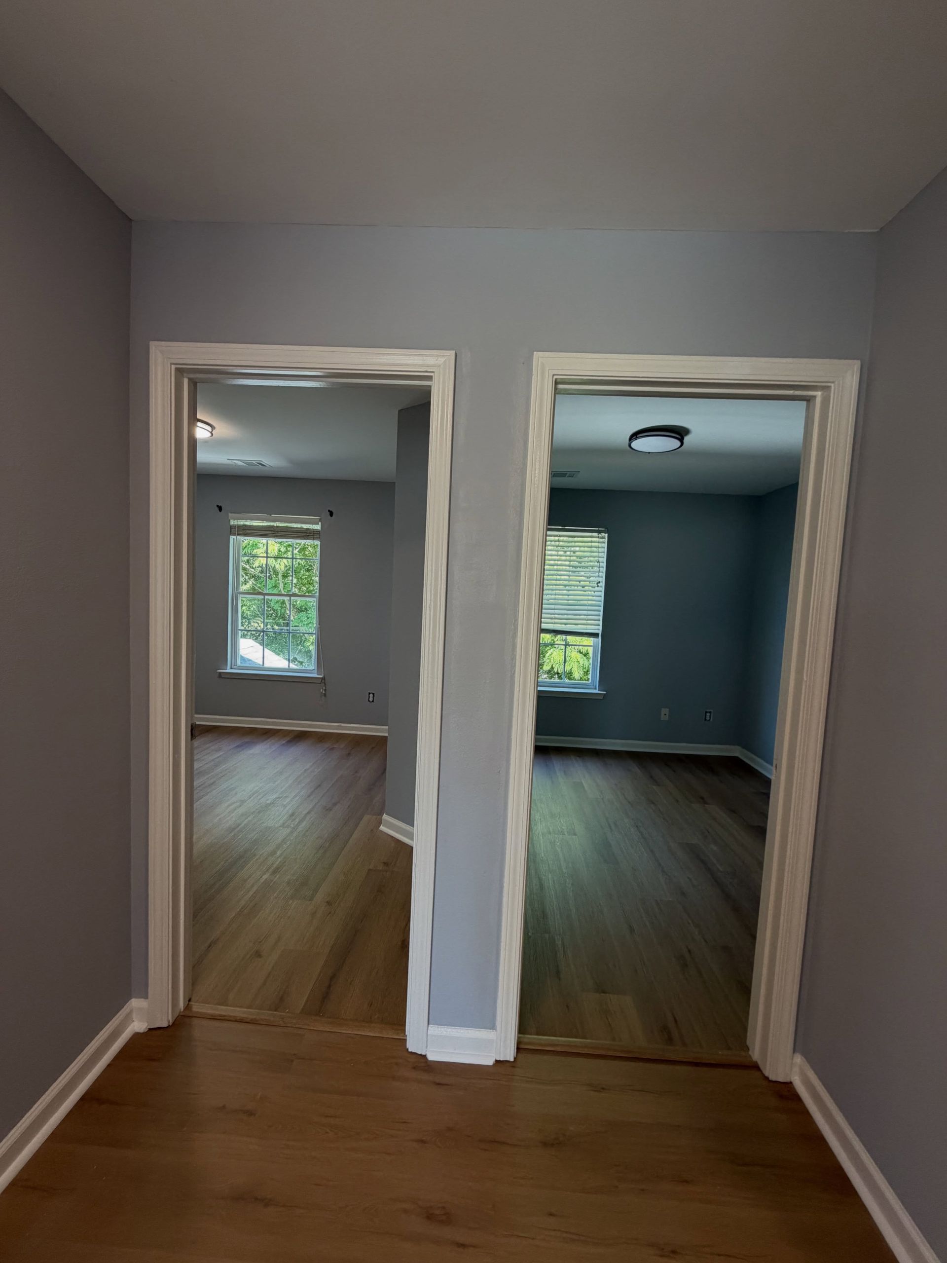 Empty hallway with two open doorways leading to wood-floored rooms, one painted blue-gray.