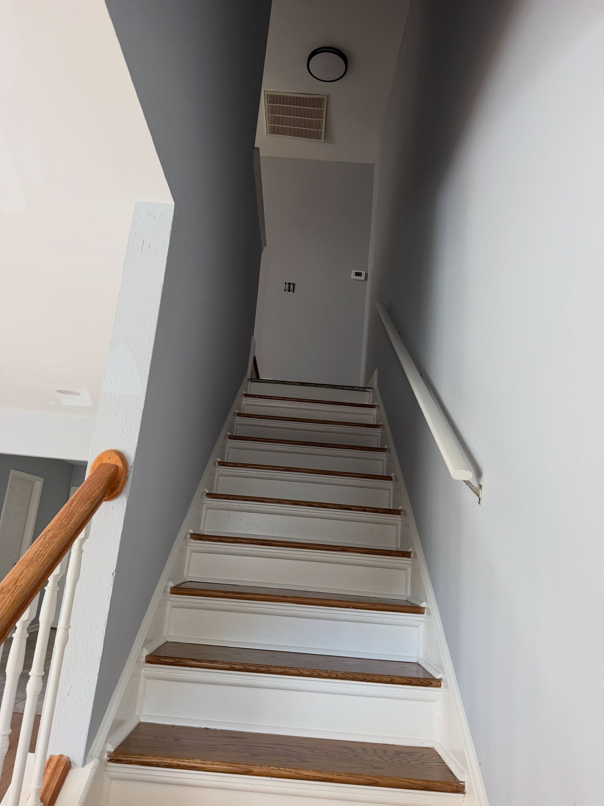 Steep indoor staircase with gray walls, wooden handrail, and a white door at the top.