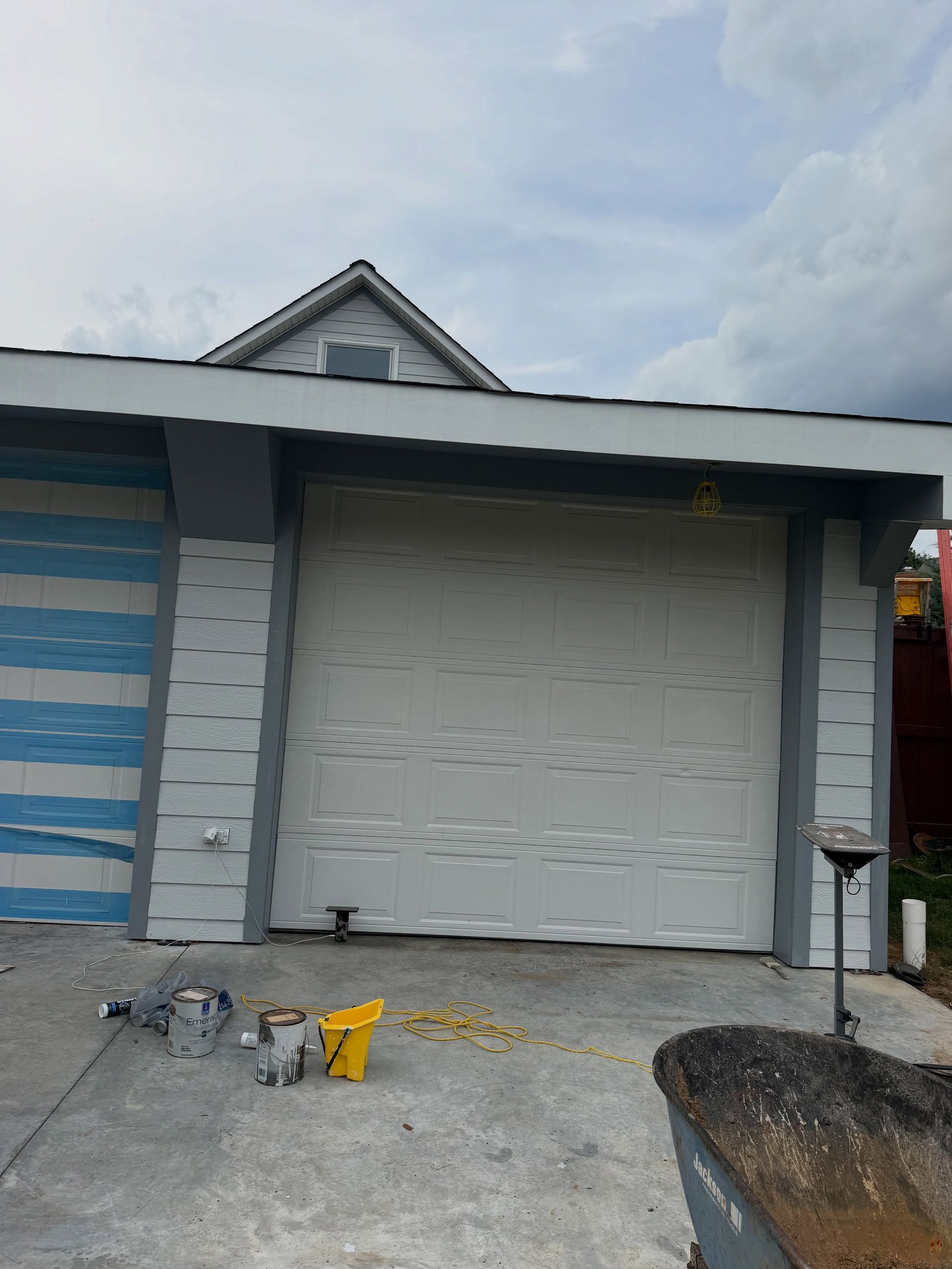 Closed garage door with scattered tools on the concrete driveway beside a striped house wall
