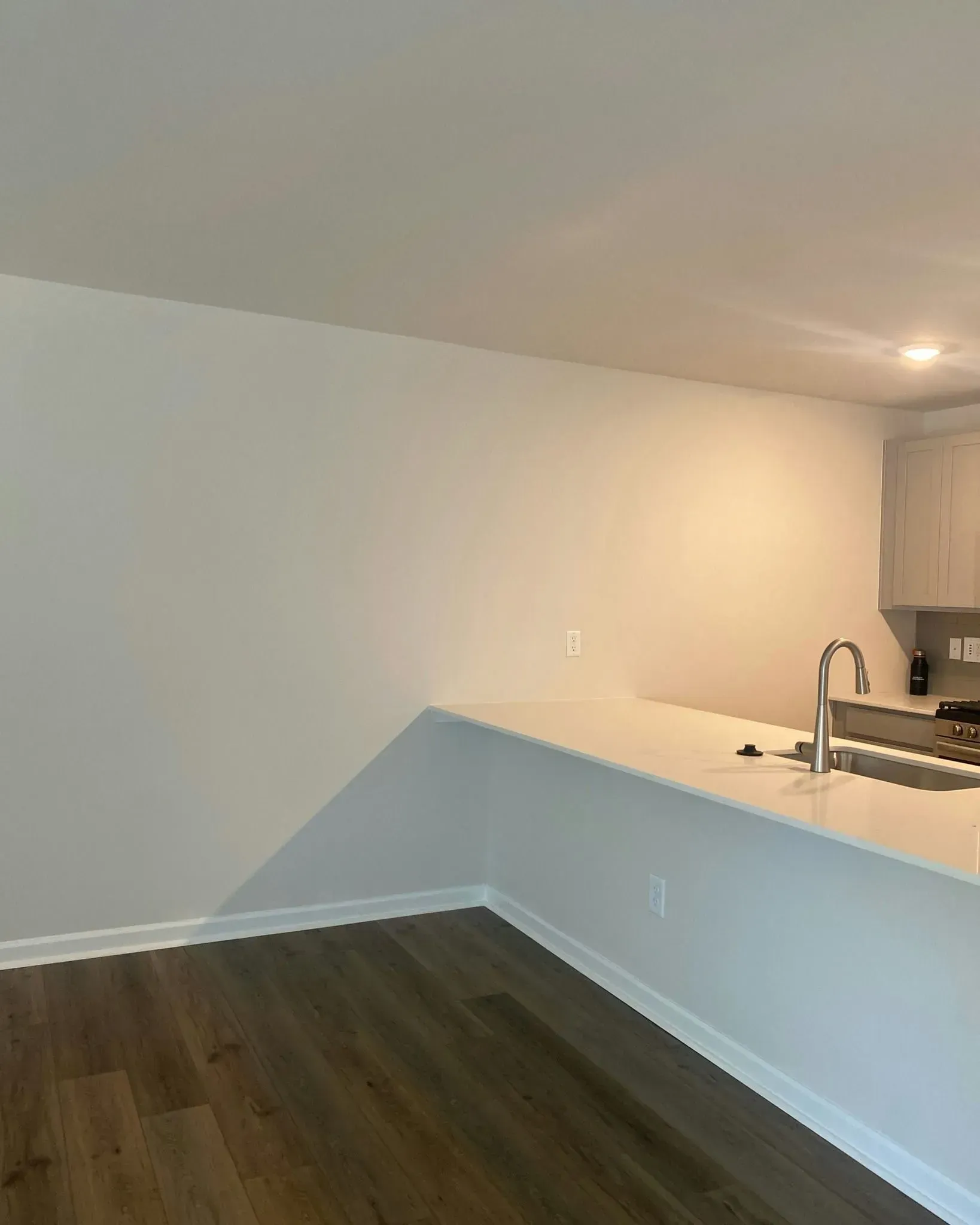 Empty modern kitchen with white island, dark wood floor, and stainless sink under warm lighting