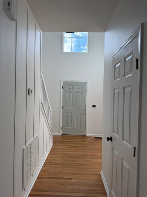 Narrow hallway with white walls, wood floor, built-in closets, and a door at the end beneath a small window.