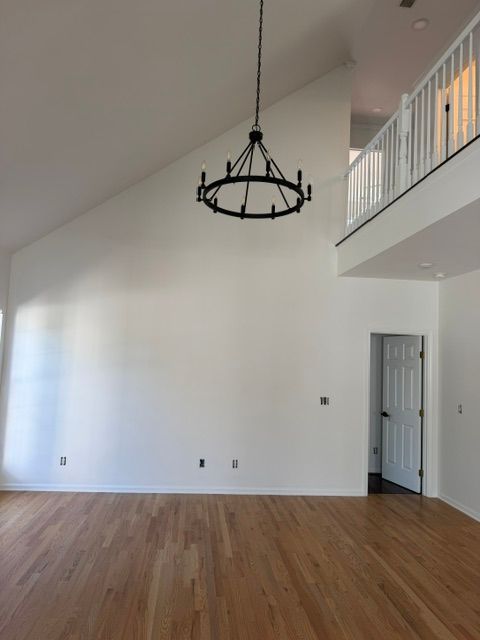 Empty modern living room with vaulted white walls, wood floors, and a black hanging chandelier