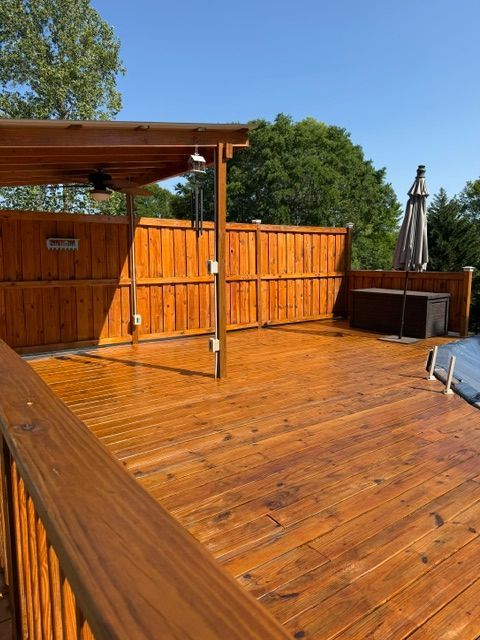 Wooden backyard deck with orange fence, pergola, and patio furniture in sunlight