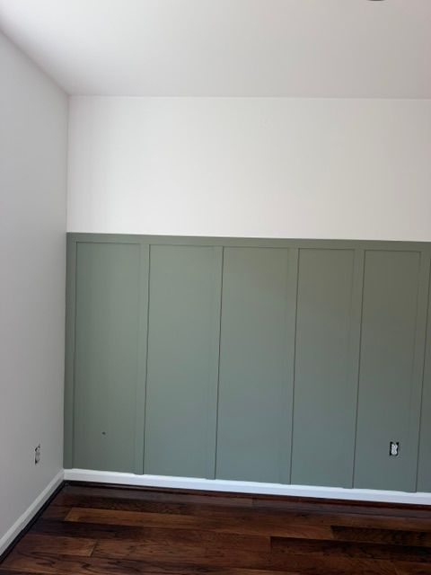 Empty room with sage green wainscoting, white walls, and dark wood flooring