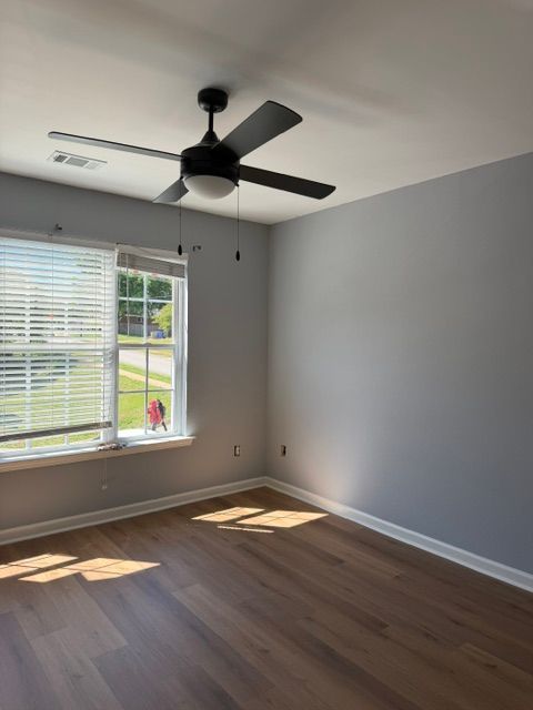 Empty room with gray walls, wood floor, ceiling fan, and sunlight through a window with blinds.