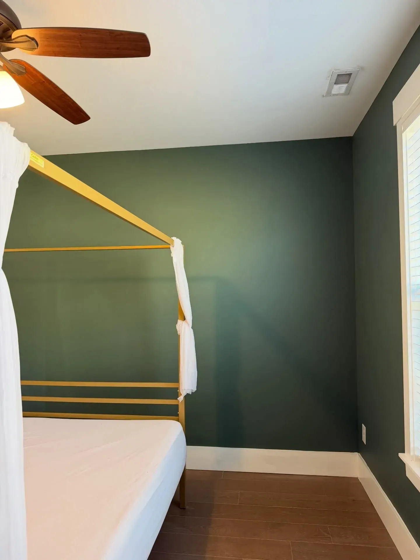 Bedroom with green walls, yellow bed frame, ceiling fan, and a window with blinds.