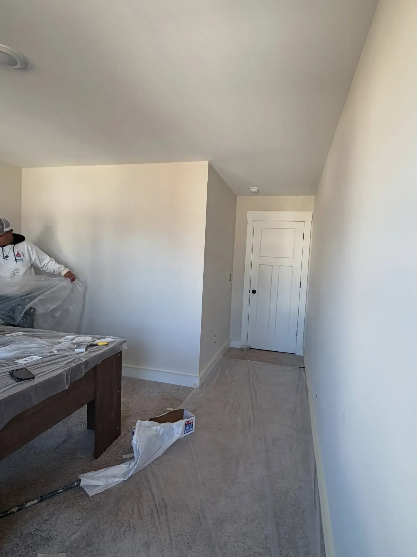 Partially furnished bedroom with a bed, plastic-covered furniture, and a white door at the back