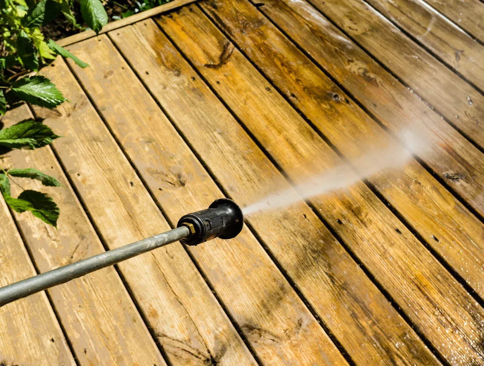 Pressure washer spraying water across a wooden deck, cleaning stained boards