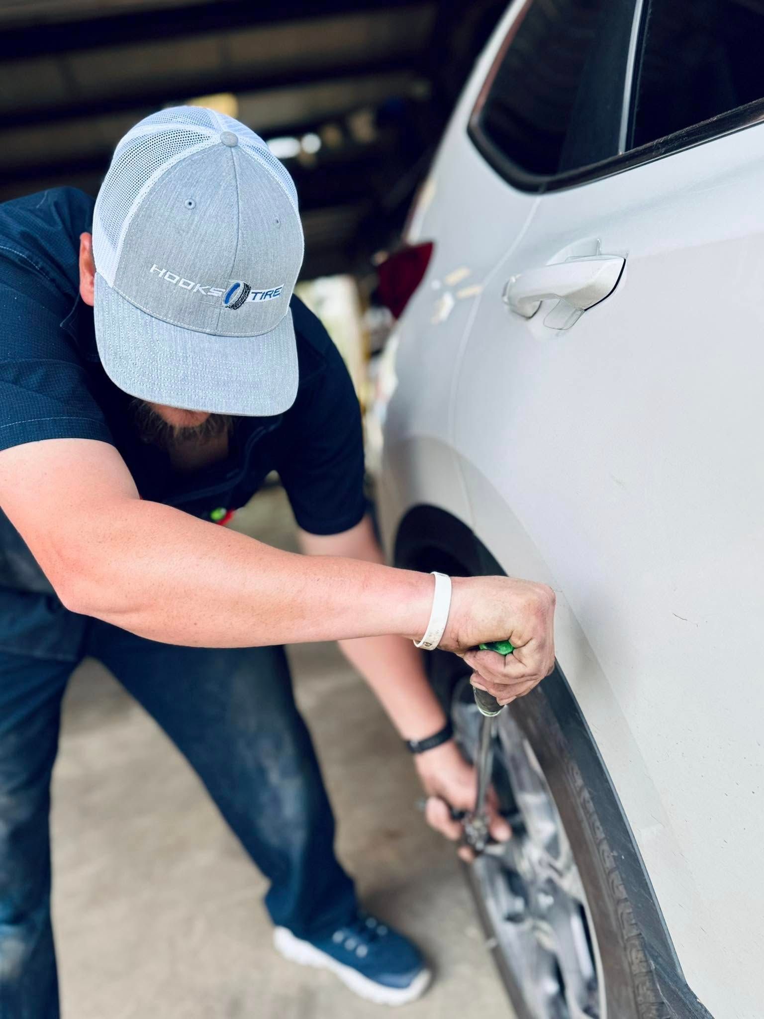Person tightening a car wheel lug nut beside a white vehicle in a garage