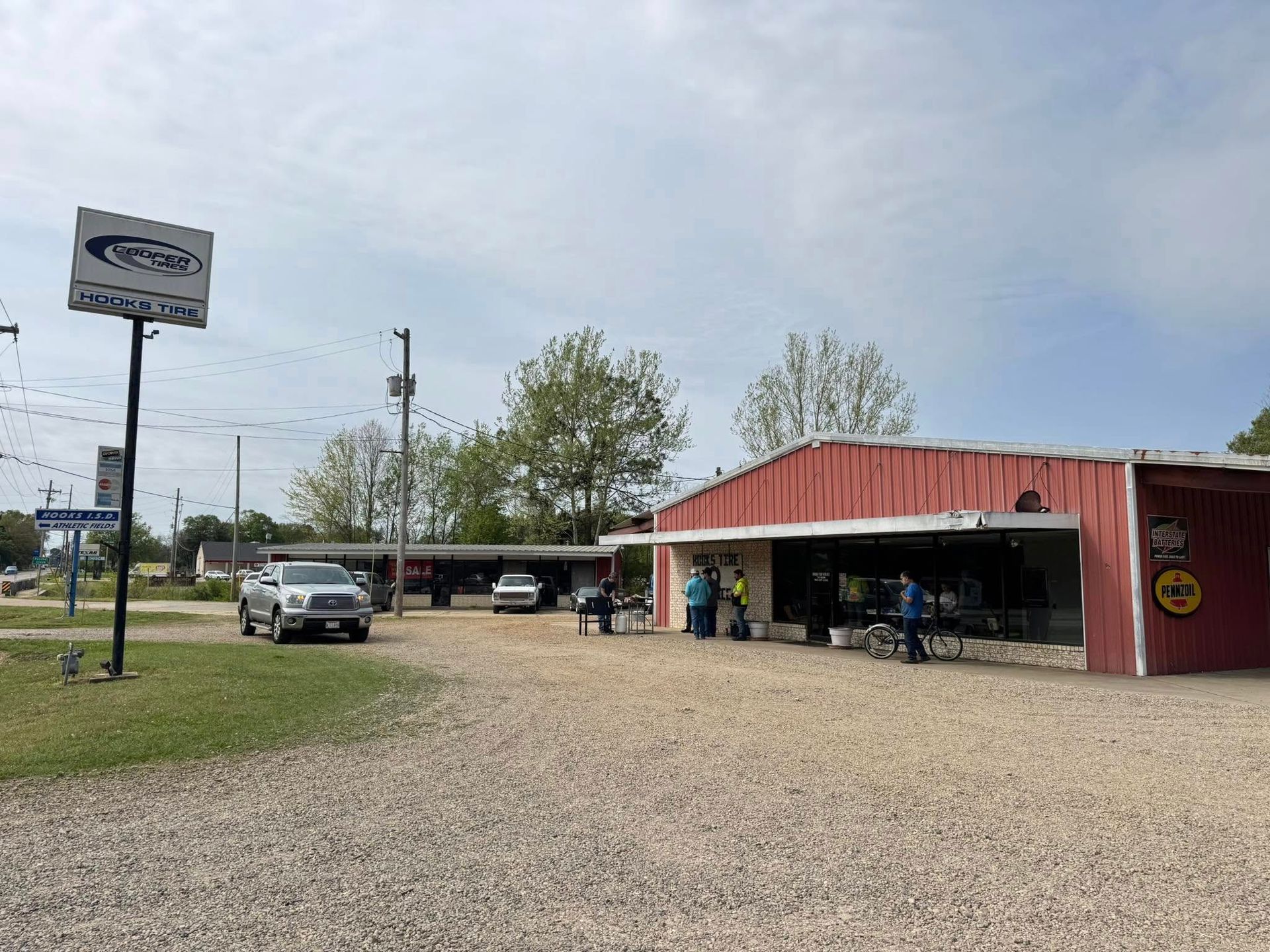 Gravel lot with a red-roofed roadside market and parked cars under a cloudy sky
