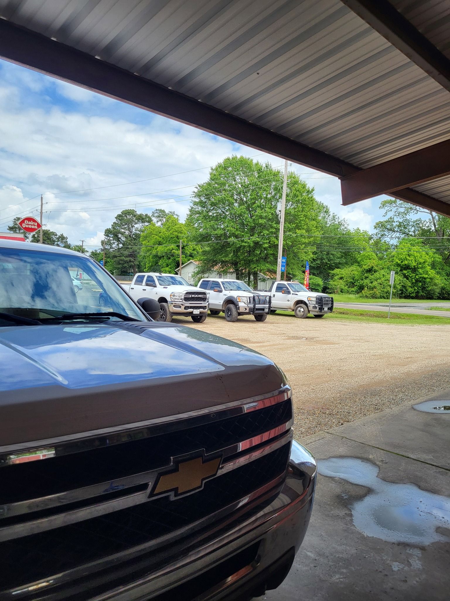 Black Chevrolet parked under a covered area, with trucks and trees in the background.