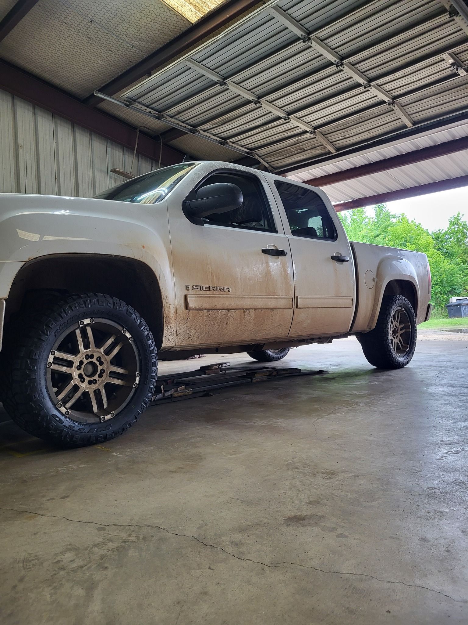 Beige pickup truck parked under a metal carport, side view.