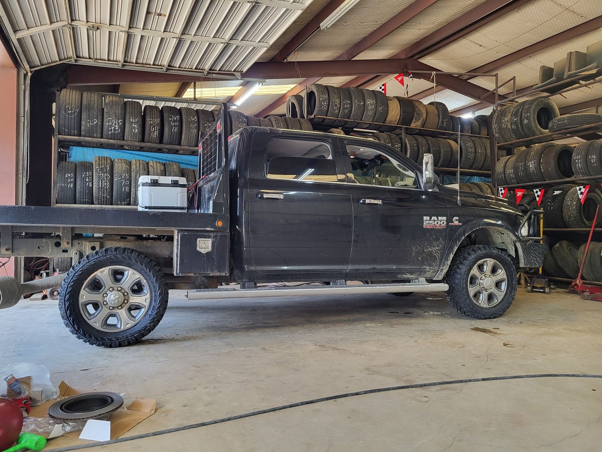 Black pickup truck parked in a tire shop garage with shelves of stacked tires and tools nearby