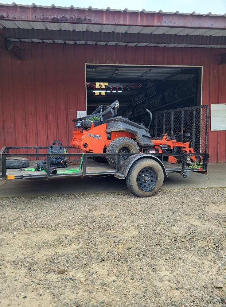 Orange zero-turn mower on a trailer in front of a red barn