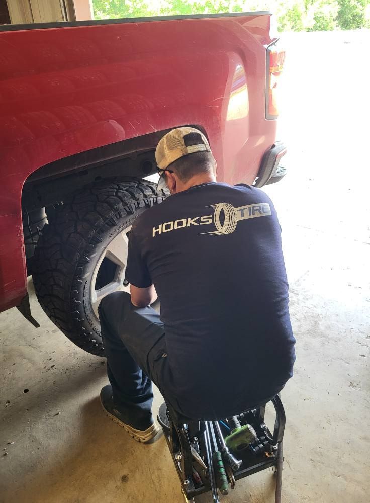 Person kneeling beside a red truck, working near the rear wheel in a garage.