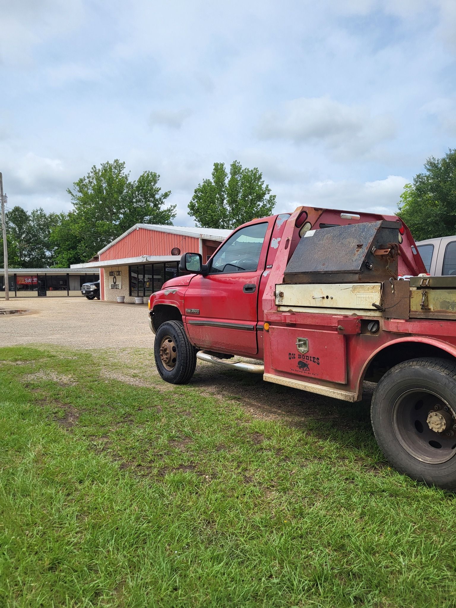 Red tow truck parked on grass near a red-roofed building under cloudy sky.